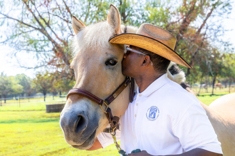 a man in a cowboy hat hugging a horse