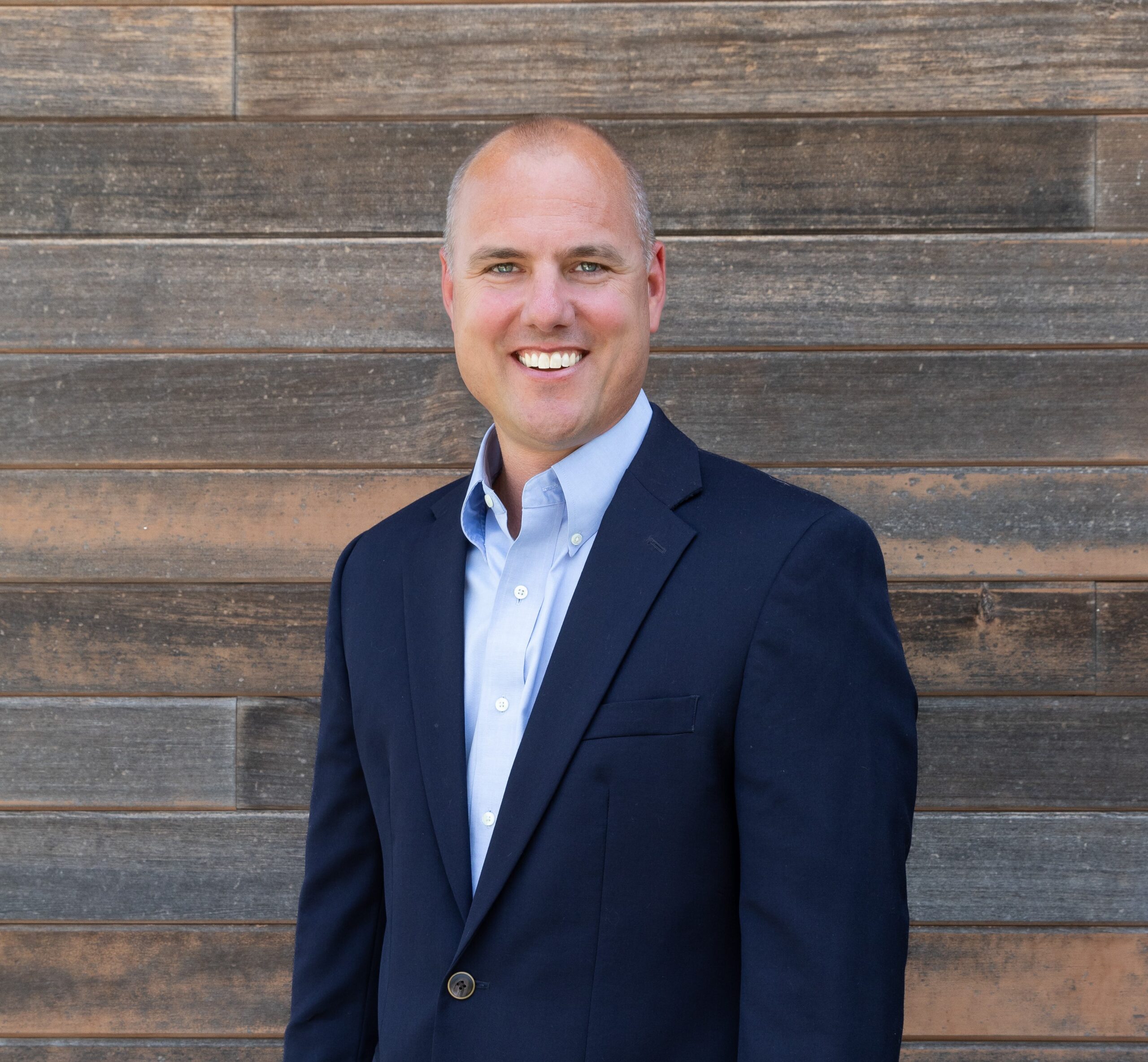 A businessman in a suit posing confidently in front of a wooden wall