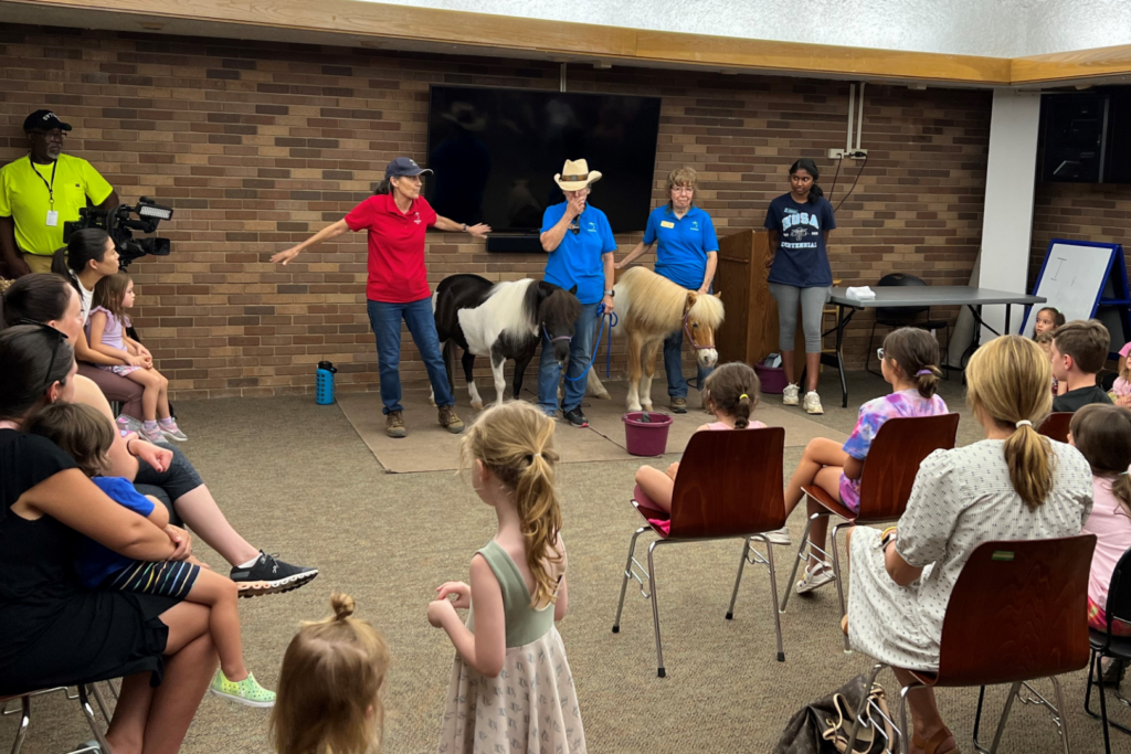 a group of people standing around a room with horses