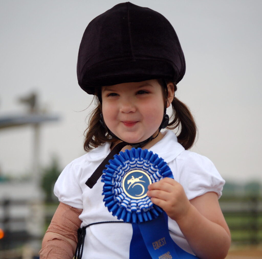 a little girl wearing a hat and holding a blue ribbon