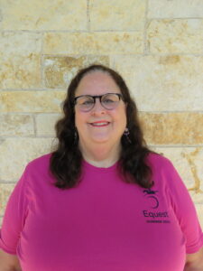 woman in a pink shirt standing in front of a brick wall