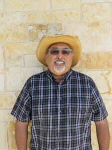 man wearing a hat and sunglasses standing in front of a stone wall