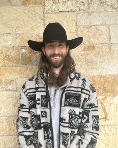 man wearing a cowboy hat standing in front of a brick wall