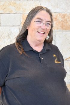 woman in a black shirt and glasses standing in front of a stone wall